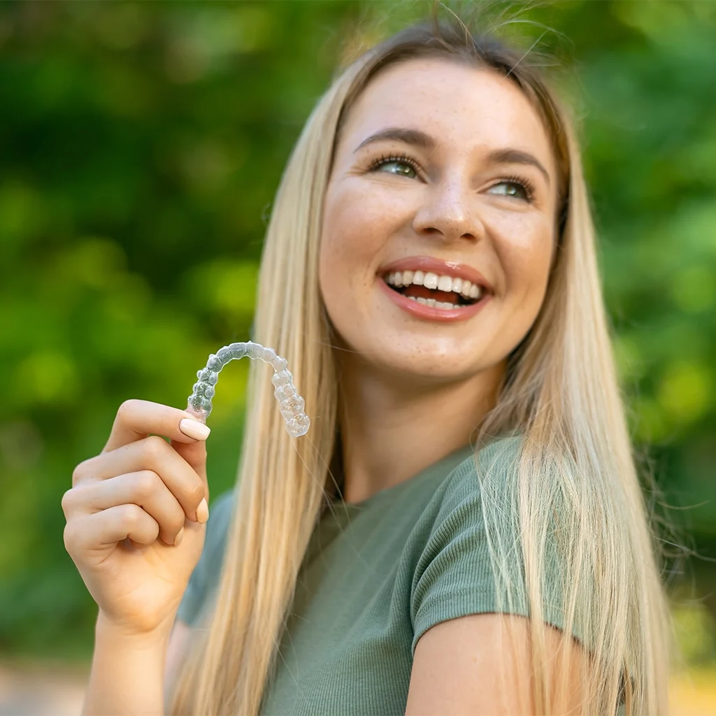 happy girl holding clear retainer outdoors and smiling
